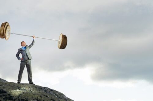 西裝男子在山頂單手舉起巨大金幣槓鈴，象徵財務槓桿的力量